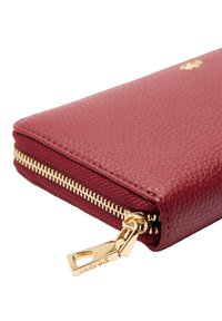 Zamszowy portfel w kolorze bordowym ze złotym zamkiem błyskawicznym i zawieszką z wygrawerowanym napisem "PARFOIS" na białym tle.