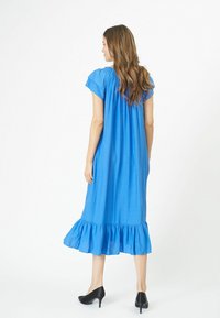 Mėlyna, iki kelių siekianti suknelė su trumpomis rankovėmis, surinktais detalėmis prie iškirptės ir plačiu volanginiu apdaila; sklandi audinio tekstūra.