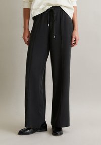 Schwarze weit geschnittene Hosen aus weichem Material, mit einem elastischen Bund und einer Kordel. Glatte Textur und minimalistisches Design.