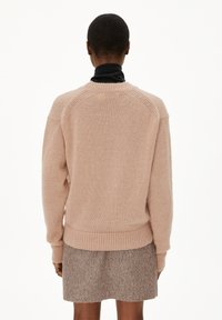 Lichtroze gebreide trui met een ronde halslijn, raglanmouwen en geribde zoom. Zachte textuur met een ontspannen pasvorm.