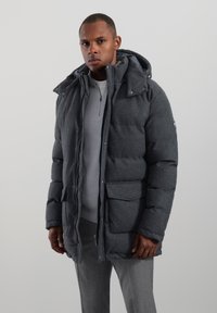 Grå puffjacka med huva, dragkedja och framfickor. Tillverkad av texturerat tyg med ett mjukt innerfoder.