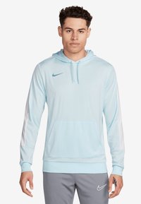 Lichtblauwe Nike-hoodie met een voorzak, verstelbare capuchon, witte zijstrepen en zilveren logo op de borst. Glad, synthetisch materiaal.