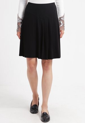 Jupe plissée noire avec une taille ajustée. Fabriquée en tissu doux, elle tombe au-dessus du genou. Associée à des ballerines noires brillantes.