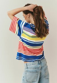 Kratek rokav, večbarvna majica s črtami v modri, rumeni, roza in rdeči barvi, kombinirana s svetlo modrimi hlačami z visokim pasom.