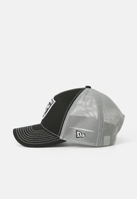 Gorra de béisbol negra y gris con parte trasera de malla, visera curvada, costuras blancas y detalles del logo en la parte delantera y lateral.