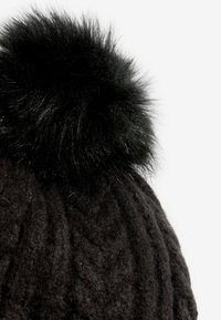 Fekete kötött sapka mintás textúrával és egy bolyhos fekete műszőrméből készült pomponnal a tetején. Az anyag puha és kényelmesnek tűnik.