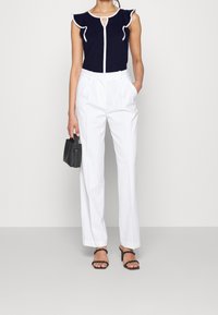 Námořnický top s volánovými rukávy a bílým lemem, detail ve tvaru klíčové dírky; bílé kalhoty na míru; černá kabelka; černé sandály se zapínáním na pásky.