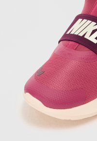 Nike sneakers i pink mesh med en glat tekstur og gummidetaljer. Har en bred maroon rem med hvid branding hen over overdelen.
