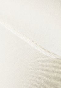 Cremefarbener Stoff mit glatter Textur und diagonalem Gewebe, versehen mit einer ordentlichen, kontrastierenden Naht als Akzent entlang der Kante.