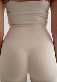 Body in tessuto a coste beige con vita alta e design senza cuciture, caratterizzato da un branding sottile impresso sul tessuto.