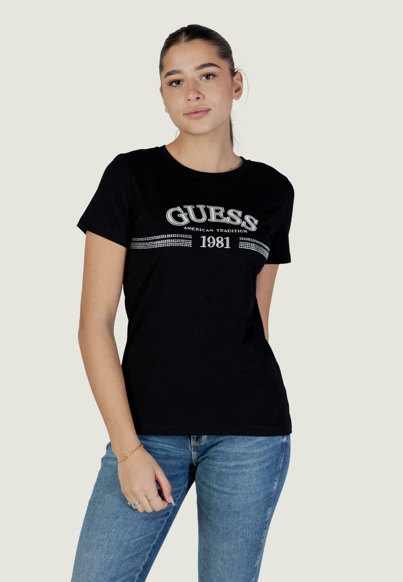 T-shirt en coton noir avec un logo argenté et un graphisme "1981" au design ajusté. Associé à un jean denim bleu clair.