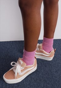 Sneakers with a pink and beige suede upper, white accents, and round laces. Paired with mid-calf pink ribbed socks.