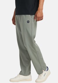 Light green sweatpants with a relaxed fit, featuring a round RVCA logo patch and side seams, paired with white sneakers.