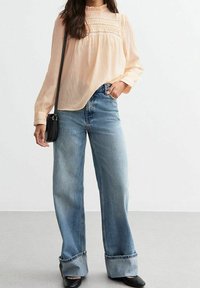 Blouse pêche claire avec empiècement texturé et manches longues, associée à un jean large taille haute en denim clair. Sac à main et chaussures noirs.