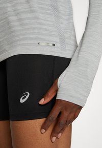 Lys grå langærmet top med struktureret mønster, parret med sorte shorts med et logo. Glat stof, tætsiddende design.