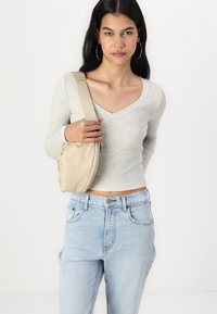 Haut à manches longues côtelé gris clair avec un col en V, associé à un jean en denim clair taille haute. Sac bandoulière beige au toucher lisse.