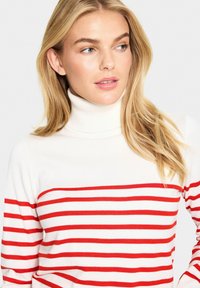 White turtleneck sweater with horizontal red stripes. Soft fabric, fitted design, and ribbed details on the neck and cuffs.
