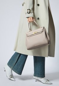 Sac à main structuré gris clair avec quincaillerie dorée et une poignée supérieure, tenu dans une main. Porté avec un trench beige et un jean évasé.