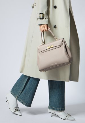 Borsa strutturata grigio chiaro con dettagli dorati e manico superiore, tenuta in una mano. Indossata con un trench coat beige e jeans a zampa.