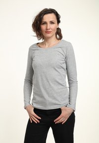 Hellgraues Langarmshirt mit Rundhalsausschnitt, weicher Textur und figurnaher Silhouette, kombiniert mit schwarzen Hosen. Minimalistisches Design.