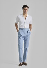 Camisa blanca de manga corta con botonadura, pantalones ligeros de corte ajustado de color azul claro con pliegues, y mocasines marrones; diseño simple y texturas suaves.