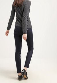 Ciemnoniebieskie, dopasowane jeansy wykonane z denimu, w połączeniu ze szarym swetrem wełnianym i czarnymi, lakierowanymi butami ze srebrnymi elementami.