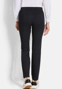 Zwarte stretchbroeken met een taps toelopende pasvorm, met een gladde textuur en een middenhoogte taille. Gepaard met bicolor sneakers voor contrast.