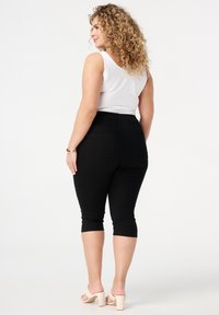 Schwarze Caprihosen mit einer figurbetonten Passform und elastischem Bund, kombiniert mit einem weißen ärmellosen Oberteil und hautfarbenen High-Heels.