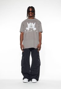 Grå oversize t-shirt med en vit fågelgrafik och texten "LOST YOUTH", kombinerad med lösa svarta cargo-byxor och vita sneakers.