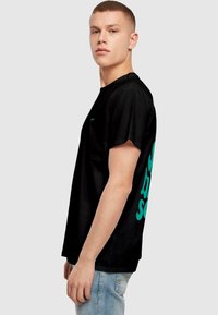 Sort bomulds T-shirt med korte ærmer, med stor aqua tekst på ryggen og et lille logo på venstre brystområde.
