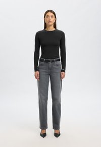 Črno dolg rokav top v kombinaciji z visokim pasom sivoh kavbojk z ravnim krojem in temnim pasom. Črni čevlji z ostro konico zaključujejo videz.