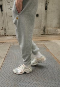 Calças de moletom cinzentas apresentam um corte descontraído com um bolso lateral. Ténis de cor clara têm painéis em malha e solas texturizadas, combinados com meias brancas.