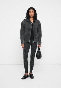 Svart denimjakke med glidelås foran, kombinert med mønstrede svarte legginger og svarte slip-on sko. Holder en liten svart håndveske.