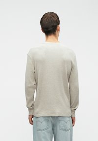 Camisola de manga longa, em cinza claro, com malha waffle, decote redondo e ajuste descontraído, combinada com jeans de denim azul claro desbotados.