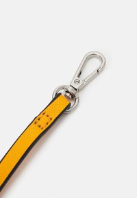 Sangle en tissu jaune avec bords noirs attachée à un mousqueton pivotant en métal argenté sur fond blanc.