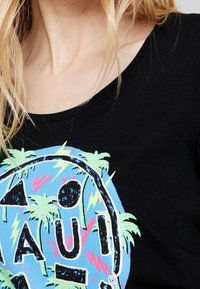 Camisa negra de manga corta con un gráfico colorido que presenta palmeras y formas geométricas sobre un fondo azul. Textura de algodón suave.