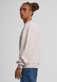 Lyserød sweatshirt med ribbet udringning og manchetter, der har en afslappet pasform og en blød struktur, parret med blå jeans.