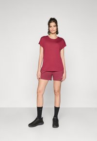 Burgunderfarget treningstopp og kortbukser sett laget av mykt stoff; kortermet, rund hals, og matchende shorts med logo detaljer. Sorte joggesko og sokker.