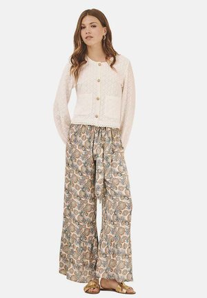 Cardigan blanco texturizado con botones dorados y dos bolsillos en la parte frontal, combinado con pantalones sueltos con estampado floral y cinta de lazo.