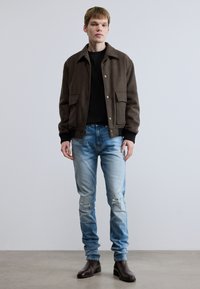 Καφέ υφασμάτινο σακάκι με δύο μπροστινές τσέπες, σε συνδυασμό με ξεβάμφο μπλε τζιν παντελόνι με φθαρμένες λεπτομέρειες και σκούρα καφέ μποτάκια στον αστράγαλο.