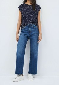 Navy blue shirt with white polka dots, short cap sleeves, paired with high-waisted, wide-leg blue jeans and white sneakers.