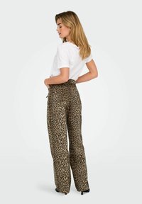 Pantalones de leopardo en beige y marrón, con un diseño de cintura alta y pierna ancha, combinados con una camiseta blanca sencilla.