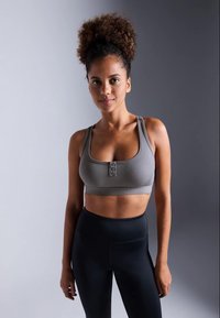Sujetador deportivo gris con un diseño texturizado y detalles de botones, combinado con leggins negros de cintura alta, todo sobre un fondo neutro.