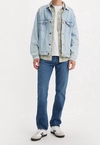 Ljusblå jeansjacka över en grön rutig skjorta, vit t-shirt, blå jeans och svart/vita sneakers. Avslappnad outfit.