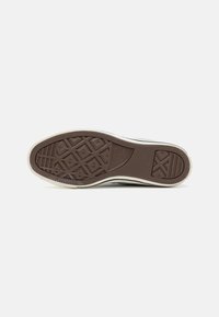 Brown rubber outsole with a textured grip pattern, circular accents, and a white midsole. Smooth design with no visible logos.