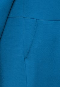 Sininen huppari, jonka kangas on sileä ja siinä on sivutasku sekä siistit saumat. Muotoilu on slim fit -tyylinen ja siinä on vain vähäisesti yksityiskohtia.