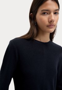 Mörkblå tröja med rundad halsringning, mjuk textur, långa ärmar och en subtil sömdetalj fram.