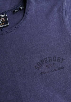 Fioletowy bawełniany T-shirt z okrągłym dekoltem i subtelną fakturą. Nadruk z napisem "Superdry NYC Athletic Essentials" w ciemnym kolorze.