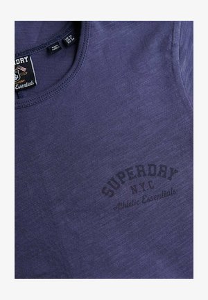 Camiseta de algodón morada con cuello redondo y textura sutil. Incluye la inscripción "Superdry NYC Athletic Essentials" en impresión oscura.