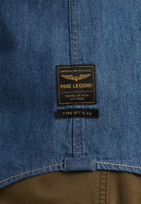 Dżinsowa kurtka o niebieskim materiale, z czarną metką z napisem "PME Legend" w złotym kolorze oraz skrzydlatym emblematem. Typ N°: C-46.